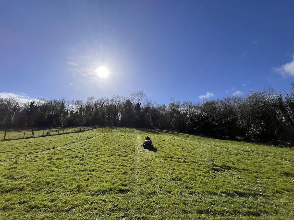 Our mower in one of the fields with the sun over the trees